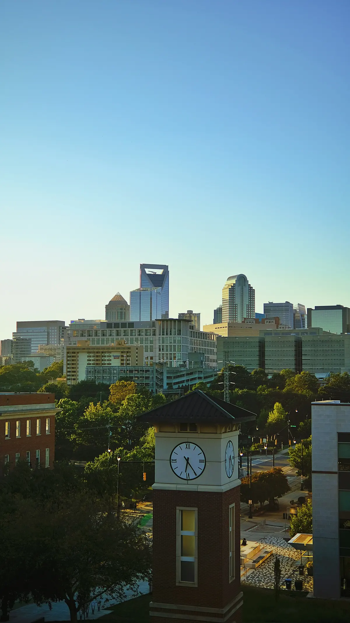 Charlotte skyline rising beyond a neighborhood clock tower under a blue sky