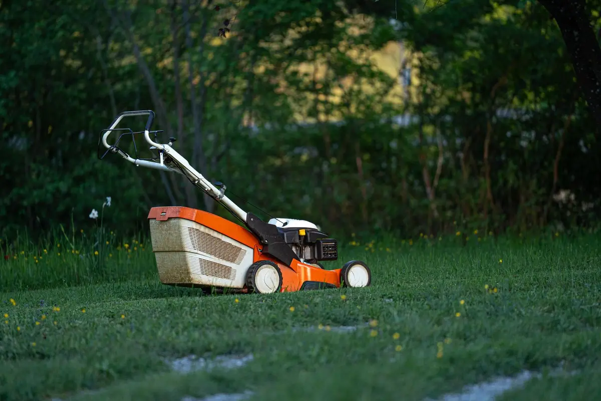 An orange push mower parked on a green lawn without an operator